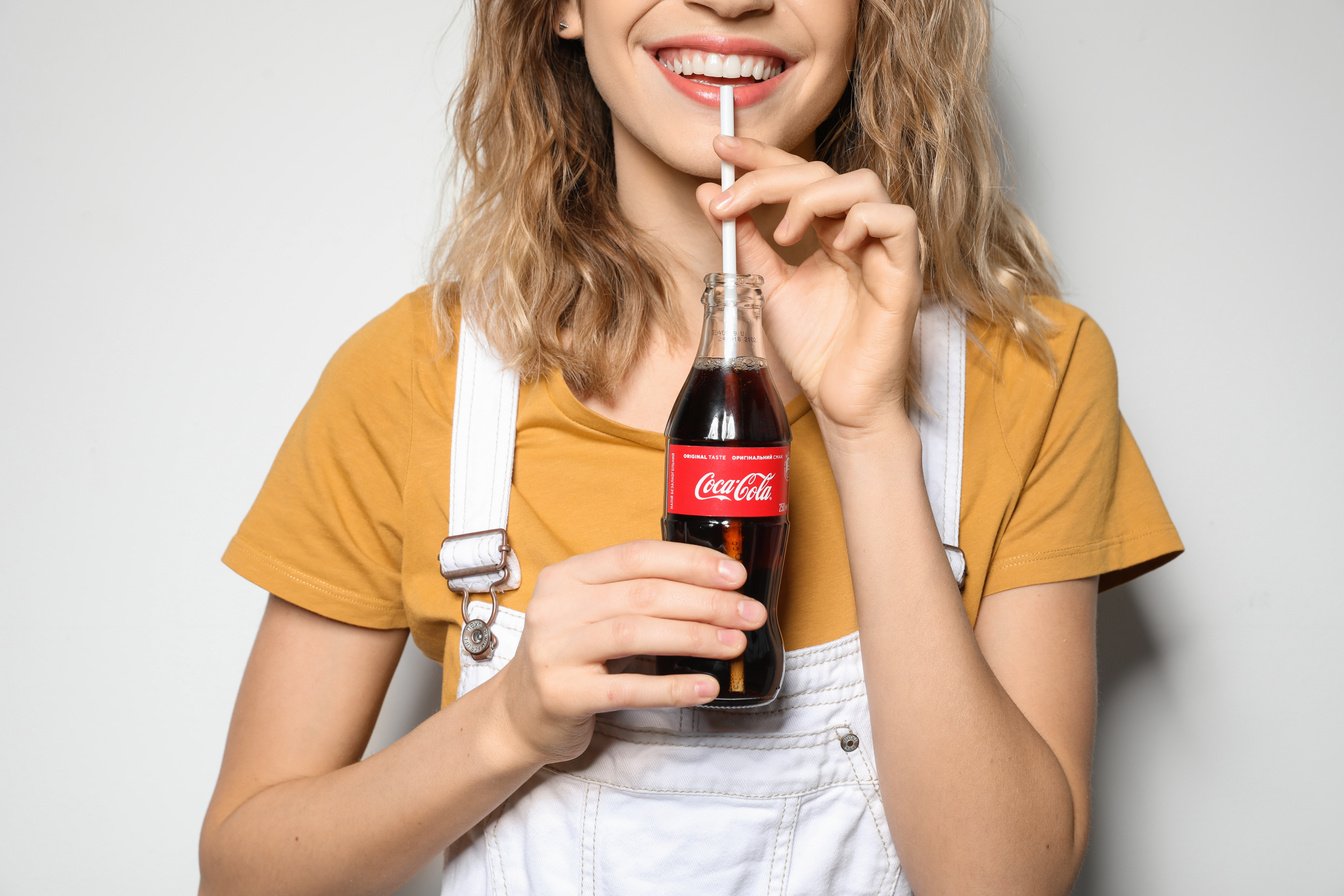 MYKOLAIV, UKRAINE - NOVEMBER 28, 2018: Young Woman with Bottle of Coca-Cola on White Background, Closeup