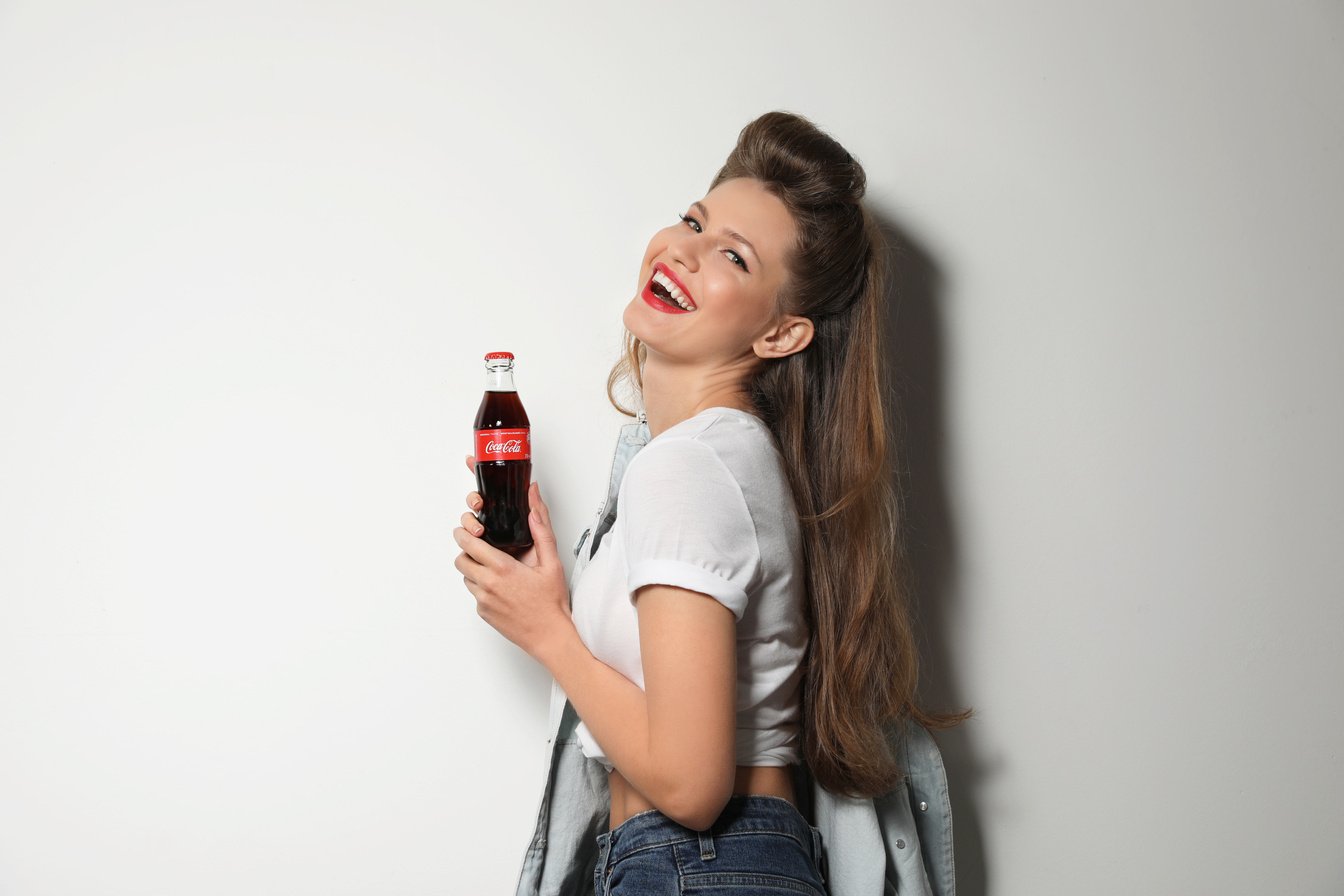 MYKOLAIV, UKRAINE - NOVEMBER 28, 2018: Young Woman with Bottle of Coca-Cola on White Background