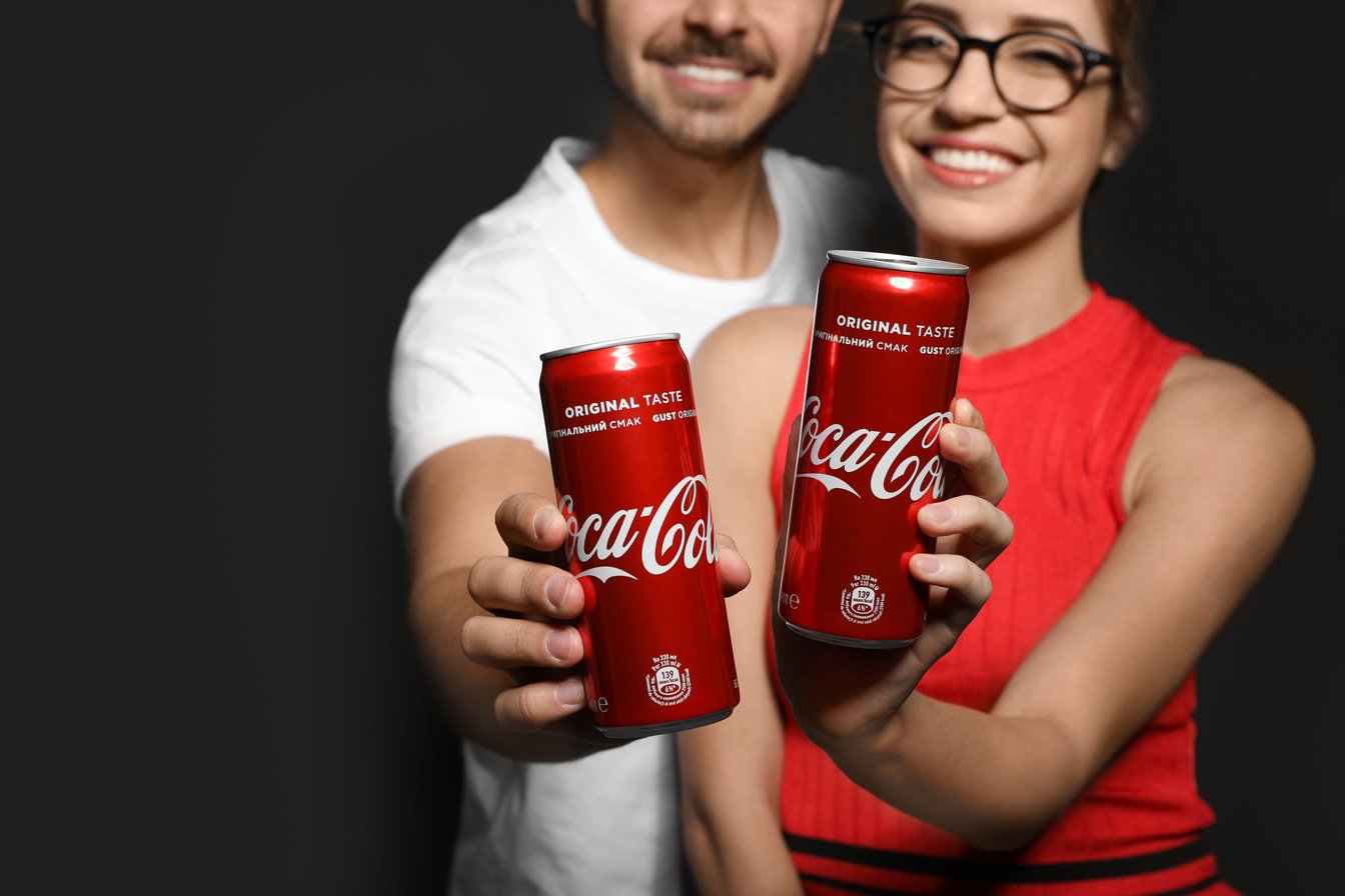 MYKOLAIV, UKRAINE - NOVEMBER 28, 2018: Young Couple with Coca-Cola Cans on Dark Background, Closeup